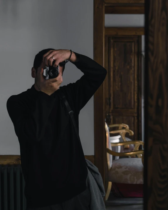 a man taking a picture of himself in a mirror, pexels contest winner, wearing jeans and a black hoodie, home album pocket camera photo, standing in a dimly lit room, lgbtq