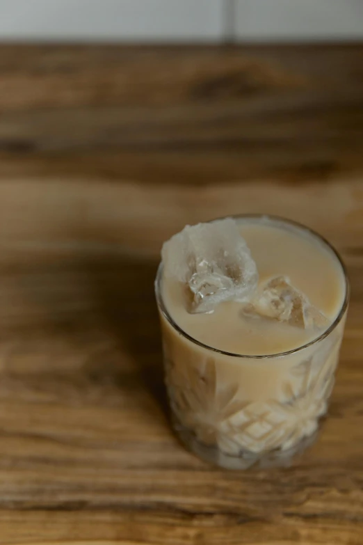 a glass filled with liquid sitting on top of a wooden table, creamy, ice, light brown, aussie baristas