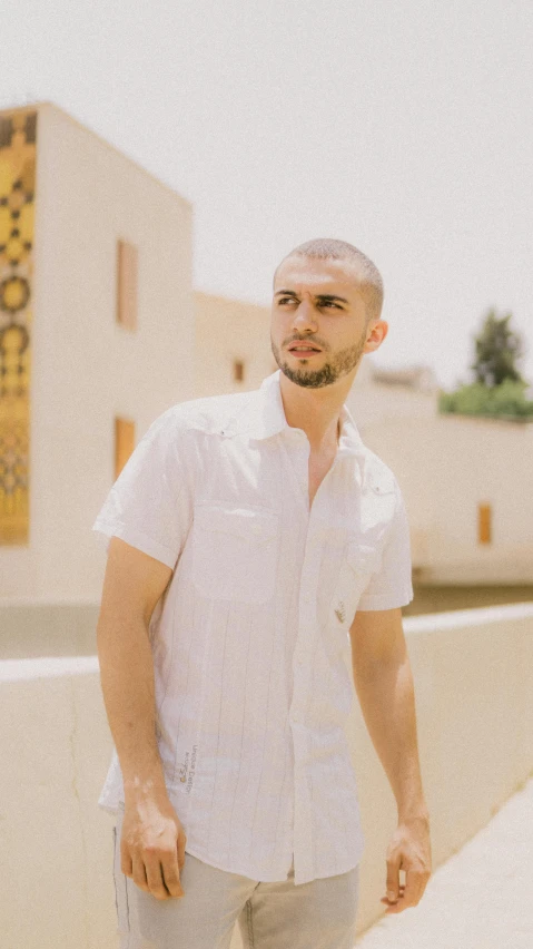 a man in a white shirt standing in front of a building, an album cover, inspired by Ahmed Yacoubi, pexels contest winner, buzz cut hair, marrakech, charli bowater, profile image
