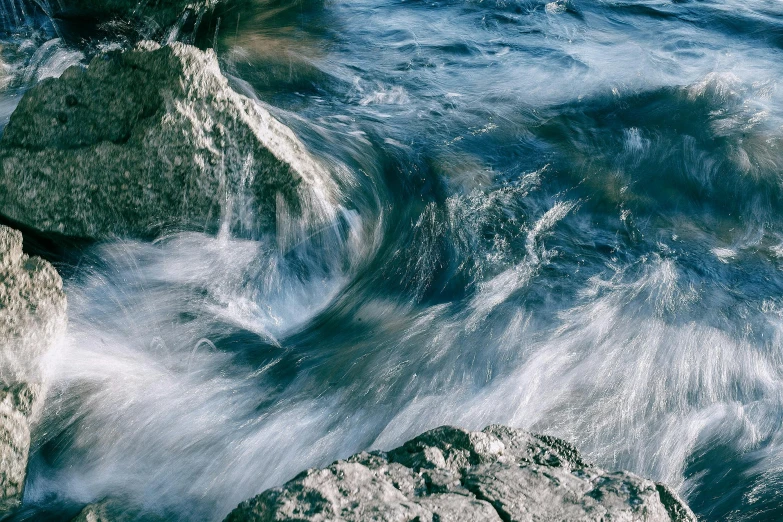 a group of rocks sitting on top of a body of water, rushing water, unsplash photo contest winner, shades of blue and grey, twisted energy flow