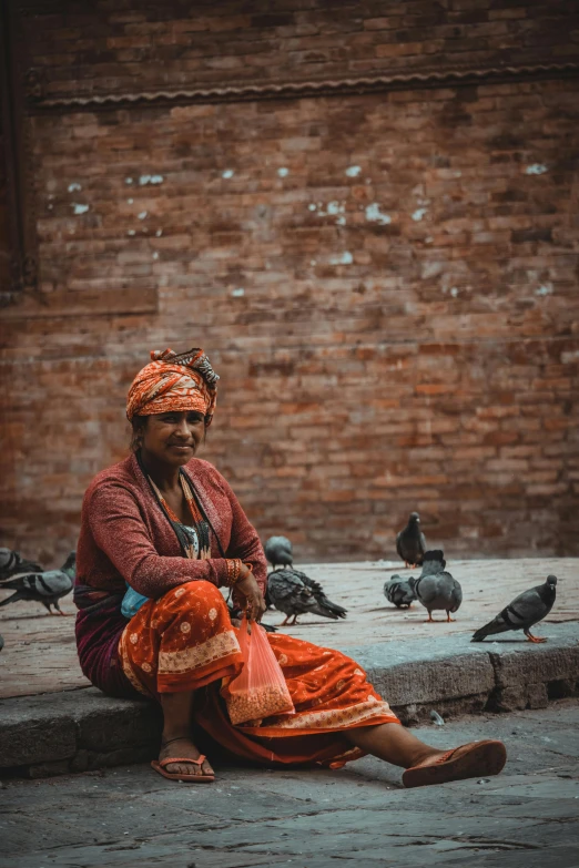 a woman sitting on a curb surrounded by pigeons, inspired by Steve McCurry, pexels contest winner, renaissance, nepal, tribal clothing, black and terracotta, color graded