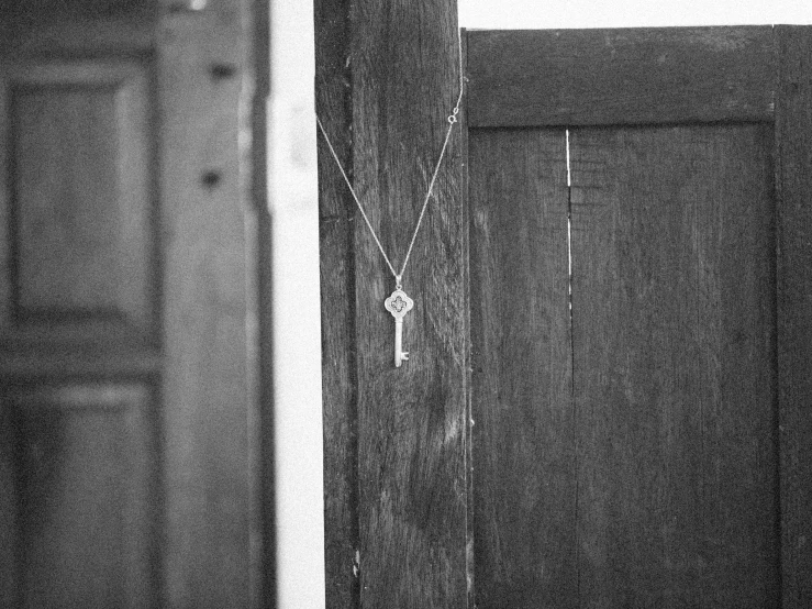 a black and white photo of a door with a key on it, unsplash, necklace on display, ffffound, vsco film grain, pendant