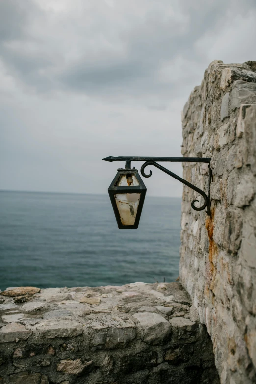 a street light hanging off the side of a stone wall, unsplash, romanticism, croatian coastline, wrought iron, black sea, stone roof