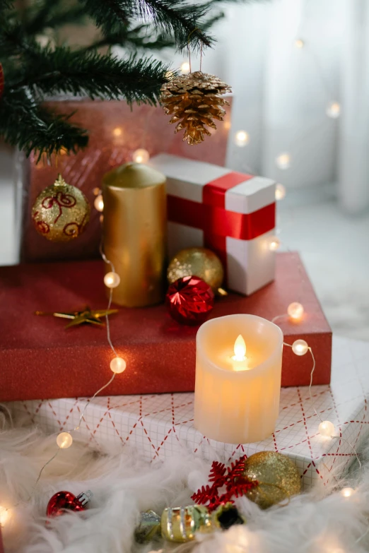 a candle sitting on top of a table next to a christmas tree, floating lights, presents, gold and red accents, ballard