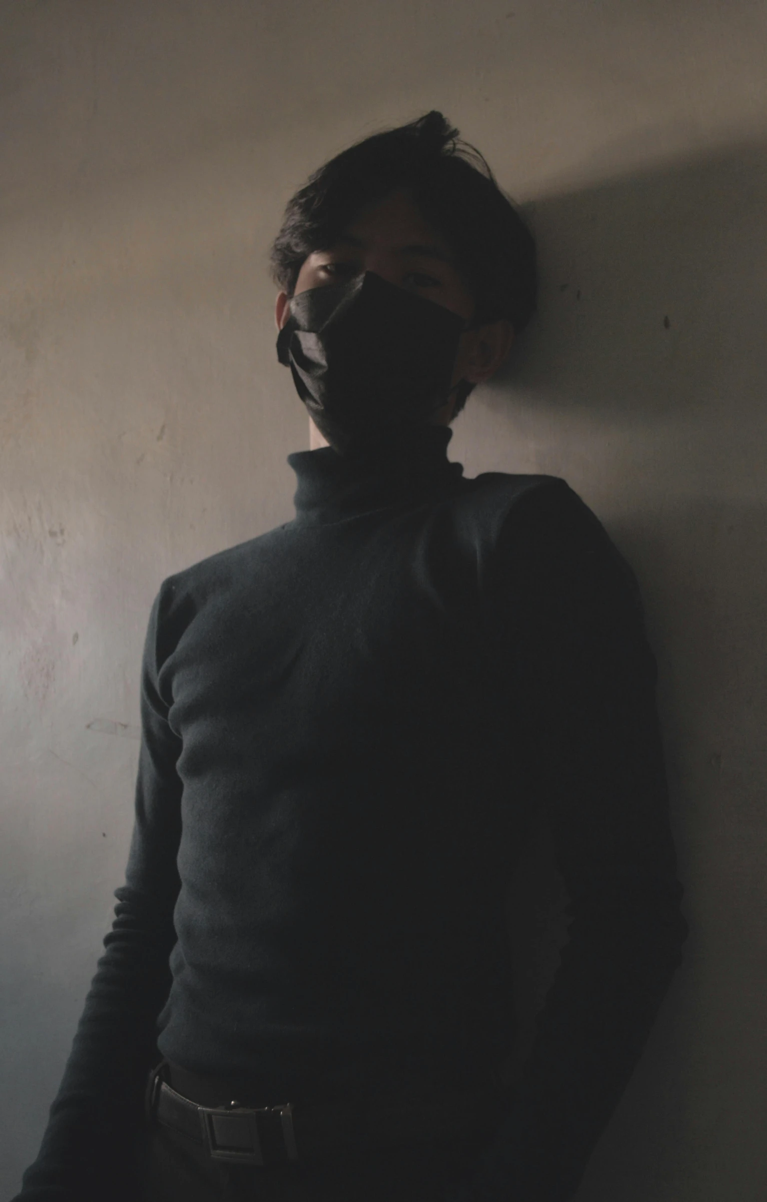 a man wearing a mask standing against a wall, black turtleneck, cinematic shot ar 9:16 -n 6 -g, ((portrait)), faded and dusty