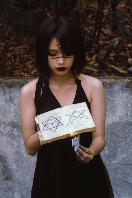 a woman in a black dress holding a book, inspired by Takato Yamamoto, featured on reddit, inscribed with occult symbols, pentagrams, photograph 3 5 mm, low quality photo