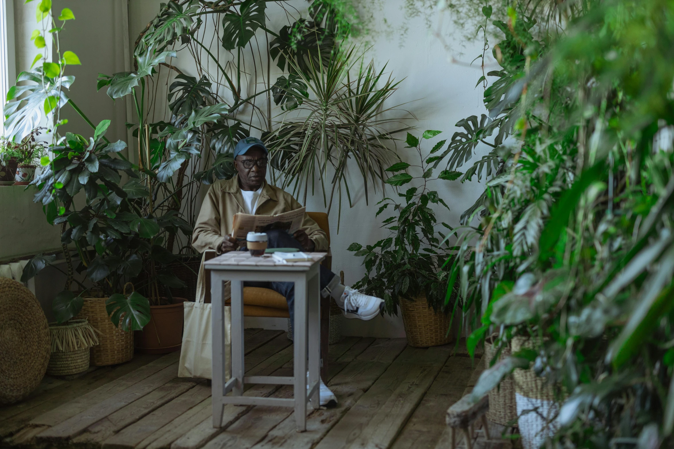 a man sitting in a chair reading a book, by Emma Andijewska, pexels contest winner, tropical houseplants, african man, people sitting at tables, against a winter garden