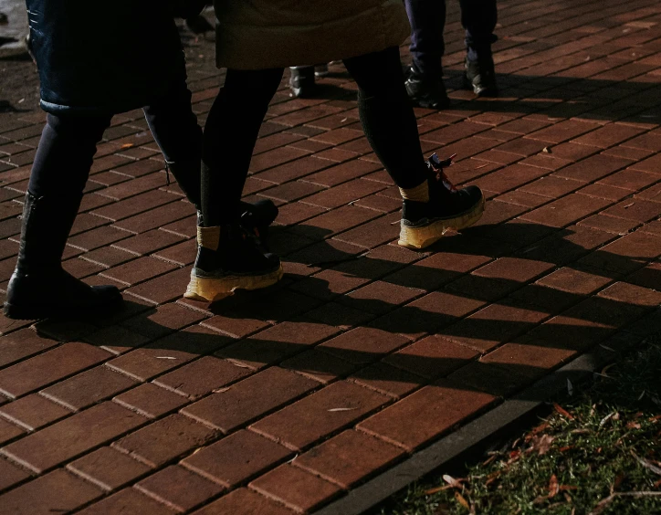 a group of people standing next to each other on a sidewalk, trending on unsplash, red bricks, detailed with shadows, walking at the park, brown