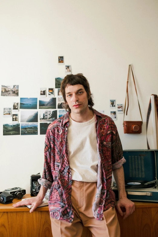 a man standing in front of a desk with a camera, an album cover, by Adam Dario Keel, portrait photo of a backdrop, heath clifford, slightly smiling, tourist photo