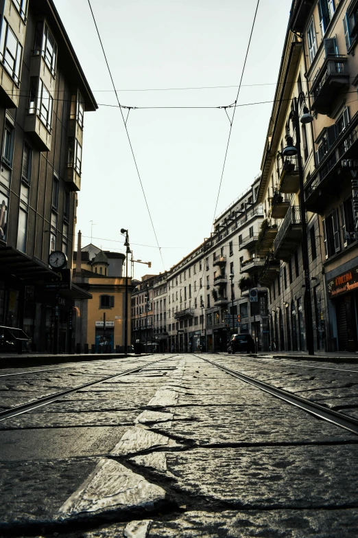 a cobblestone street in a european city, an album cover, by Patrick Pietropoli, pexels contest winner, milan schere, trams ) ) ), empty metropolitan street, buildings covered in black tar