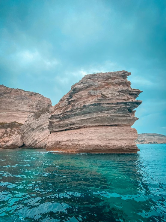 a rock formation in the middle of a body of water, light blue water, sharp cliffs, profile pic, stacked image