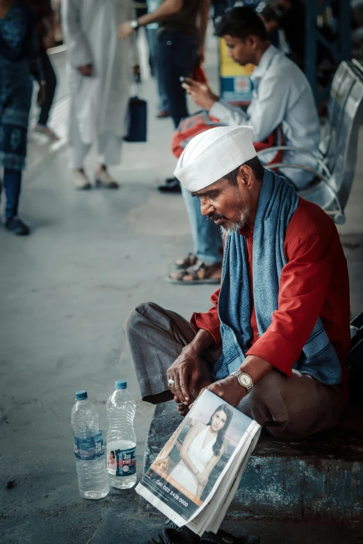 a man sitting on a bench reading a book, a picture, inspired by Steve McCurry, pexels contest winner, hyperrealism, old dhaka, baggy clothing and hat, a group of people, man with a blue heart