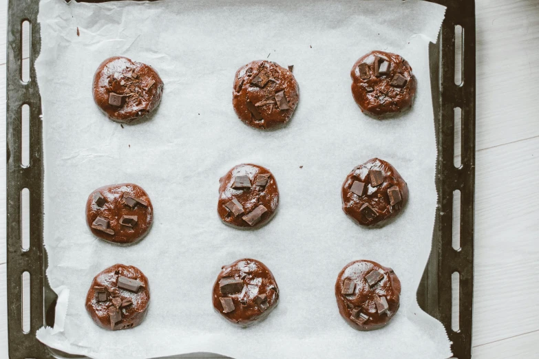 a pan filled with chocolate cookies on top of a table, by Julia Pishtar, trending on pexels, process art, wet amphibious skin, parchment paper, glazed, bombs