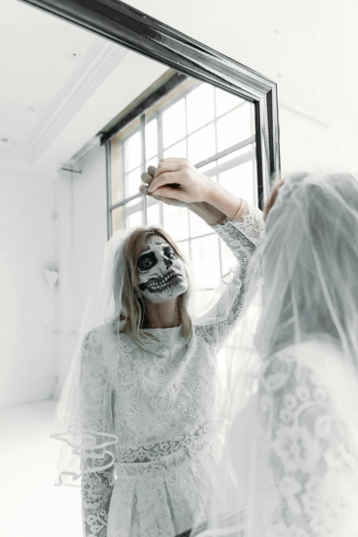 a woman that is standing in front of a mirror, a black and white photo, inspired by Elsa Bleda, trending on unsplash, skull face paint, wearing a wedding dress, with a white background, halloween celebration