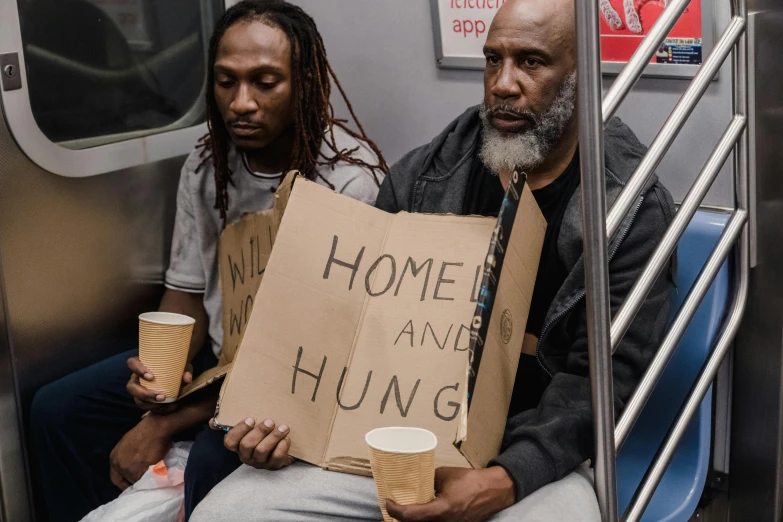 two people sitting on a subway holding signs, by Dan Frazier, pexels contest winner, renaissance, hungry, shanty town, at home, in new york city