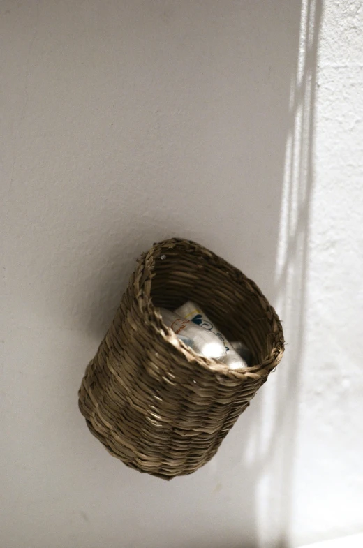 a basket hanging on a wall next to a toilet, by Nina Hamnett, happening, newspaper, on a candle holder, hay, eye - level view