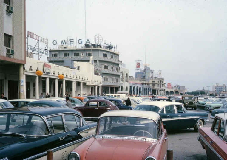 a street filled with lots of cars next to tall buildings, a colorized photo, 1960s american world's fair, at the seaside, vintage aston martin, omega