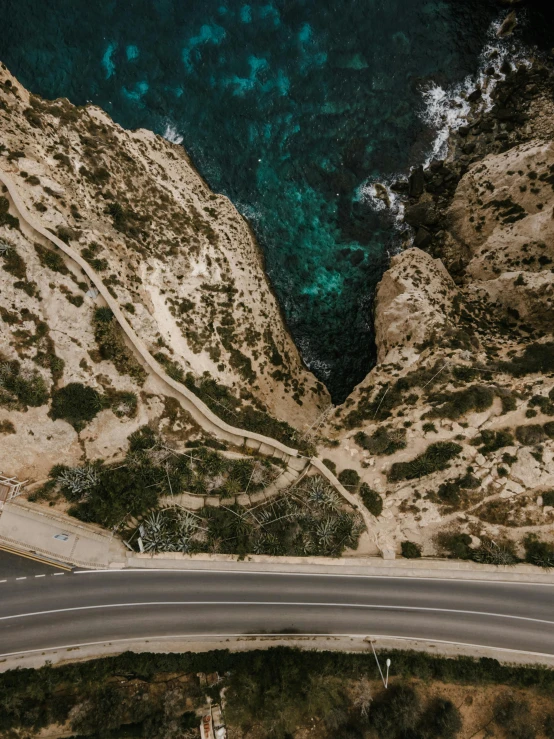 an aerial view of a winding road next to the ocean, pexels contest winner, les nabis, sharp cliffs, top view of convertible, low quality footage, over a calanque