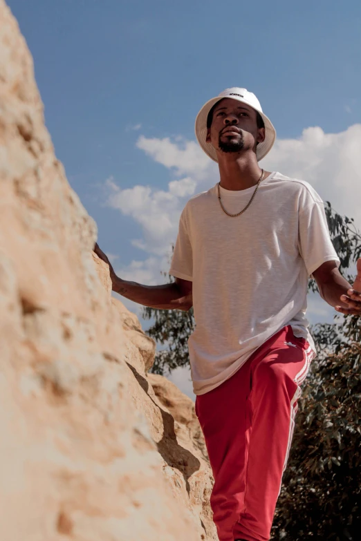 a man standing on top of a rock next to a tree, by Afewerk Tekle, happening, bucket hat, red sport clothing, zoomed in shots, wearing off - white style