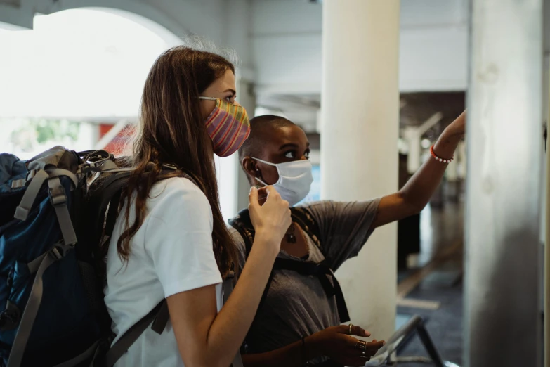 a couple of people standing next to each other, pexels contest winner, interactive art, medical mask, black. airports, woman holding another woman, student