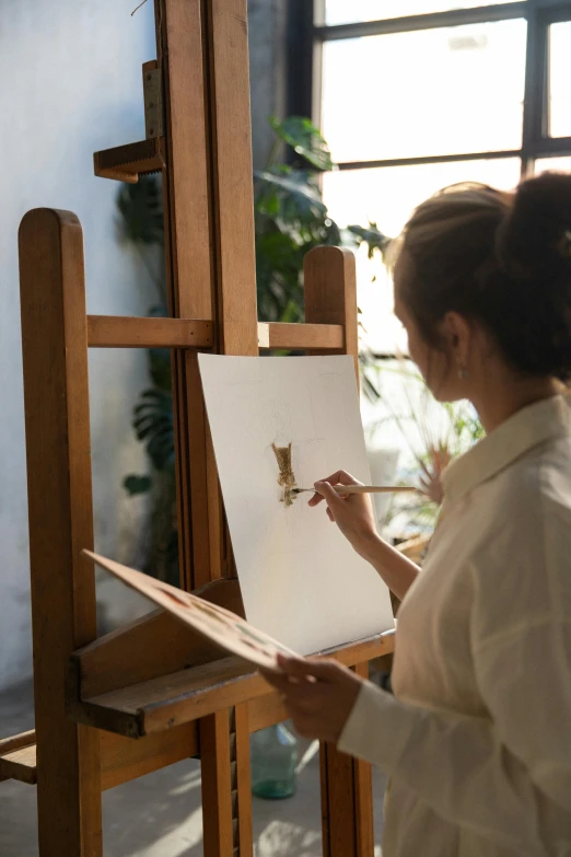 a woman that is standing in front of a easel, pexels contest winner, academic art, holding a paintbrush, afternoon sunlight, indoor scene, furry artist