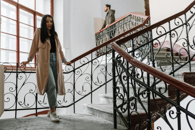 a woman standing at the top of a set of stairs, a picture, by Emma Andijewska, pexels contest winner, lyco art, light brown trenchcoat, two models in the frame, handsome girl, inside the building