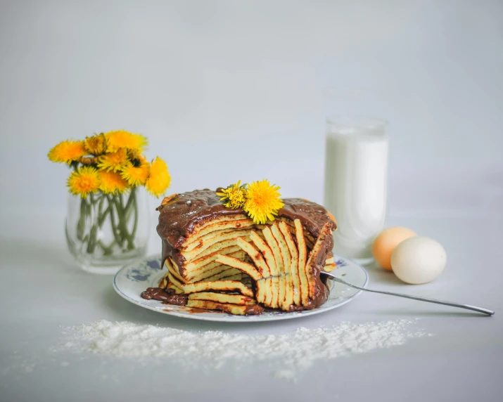 a cake sitting on top of a plate next to a glass of milk, many golden layers, with yellow flowers around it, folded, rib cage exposed