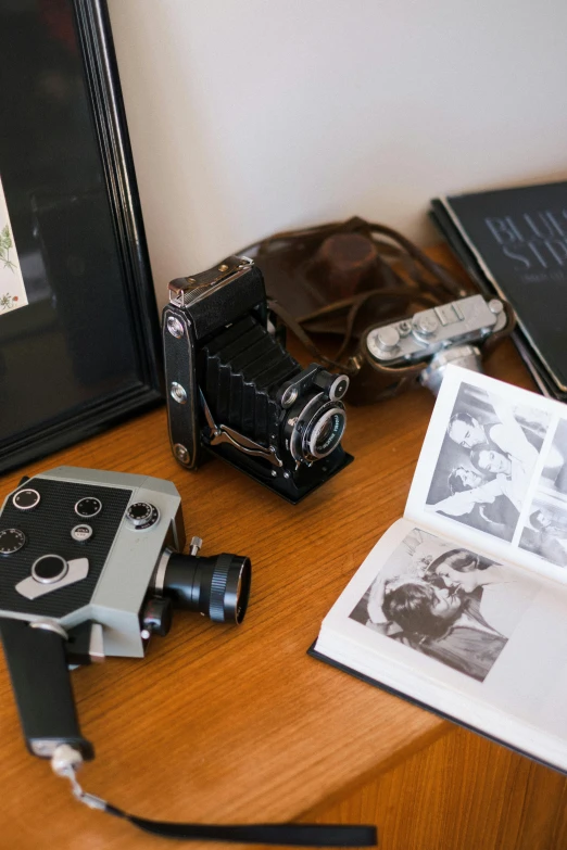 a camera sitting on top of a wooden table next to a book, a still life, visual art, picture frames, old hollywood themed, on desk, dwell