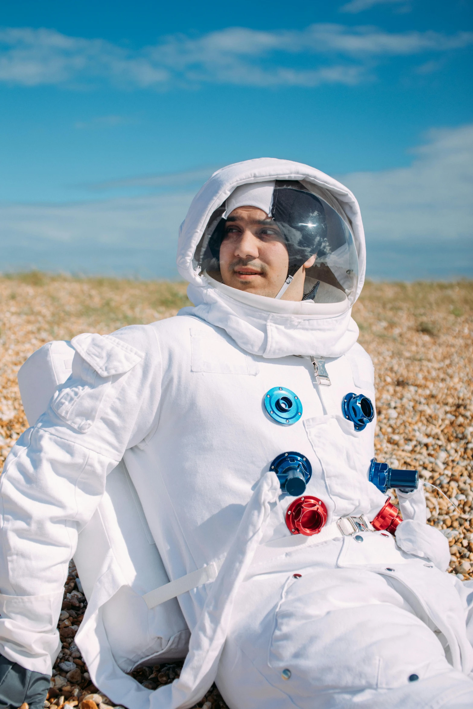 a man in an astronaut suit sitting on a beach, robert sheehan, rex orange county, fancy dress, spacehip lands