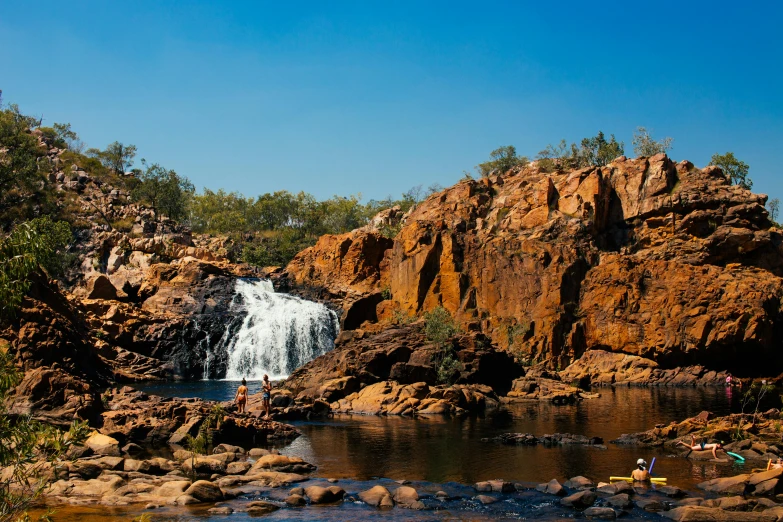 a group of people standing in front of a waterfall, by Elizabeth Durack, pexels contest winner, panoramic, aboriginal capirote, fishing, beautiful sunny day