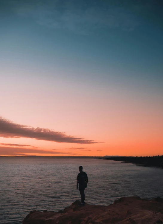 a person standing on a rock in front of a body of water, on the beach during sunset, human staring blankly ahead, lachlan bailey, today\'s featured photograph 4k