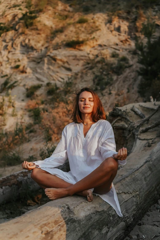 a woman in a white shirt is sitting on a log, trending on unsplash, renaissance, lotus pose, wearing a robe, maxim shirkov, cliffside