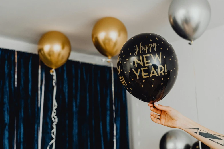 a person holding a balloon that says happy new year, by Julia Pishtar, trending on pexels, gold and black blu, decoration, navy, heath clifford