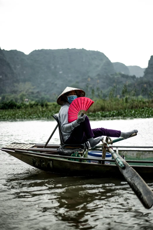 a person sitting in a boat with a fan, inspired by Steve McCurry, in style of lam manh, sustainability, mountains and rivers, 2022 photograph