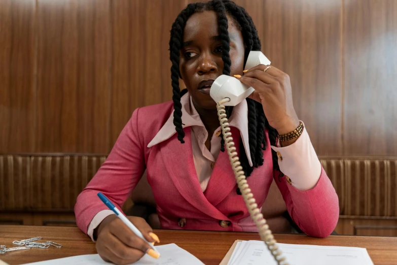 a woman sitting at a table talking on a telephone, pexels contest winner, brown and pink color scheme, black teenage girl, business attire, unedited