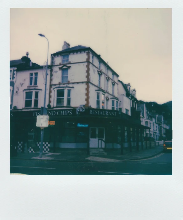 a large white building sitting on the side of a road, a polaroid photo, by Nick Fudge, unsplash, private press, old shops, low quality instant camera photo, hot food, wales