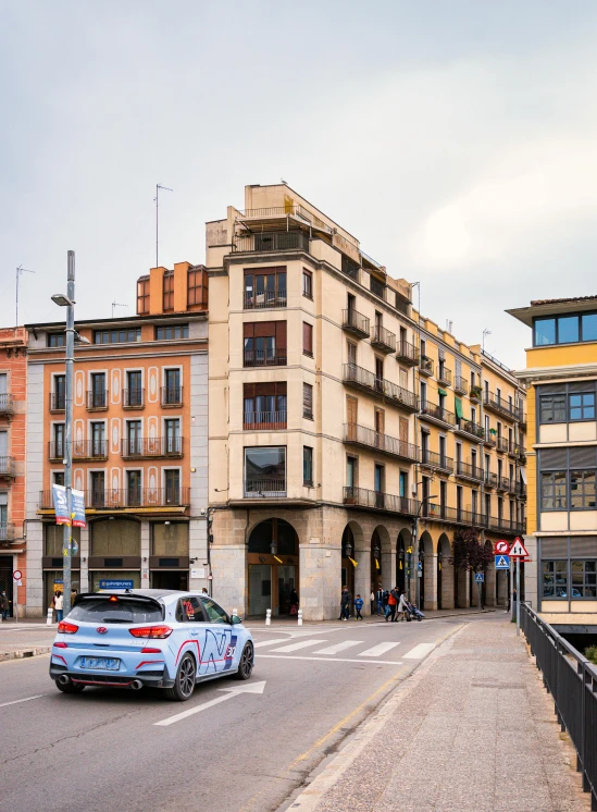 a car driving down a street next to tall buildings, inspired by Lajos Berán, pexels contest winner, hyperrealism, arrendajo in avila pinewood, neoclassical police station, high resolution photograph, square