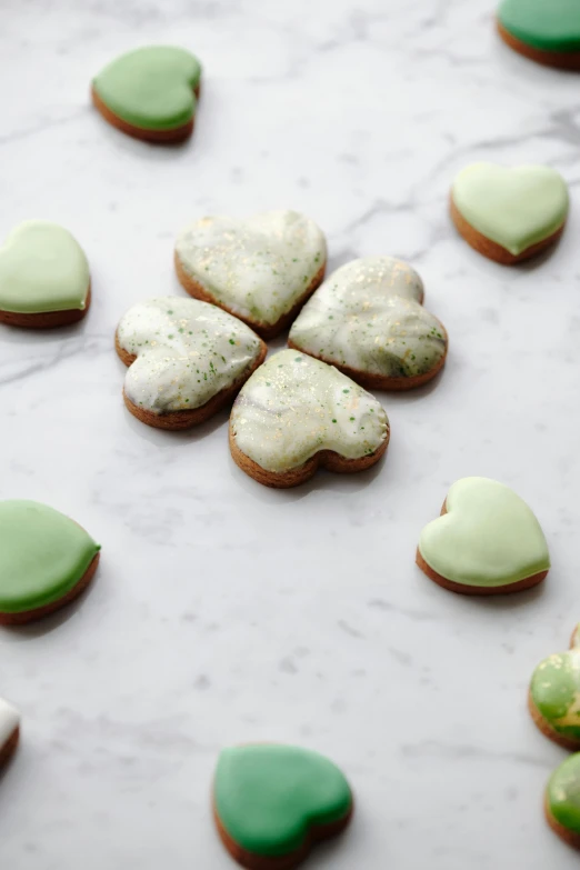 a table topped with lots of green and white cookies, inspired by Christen Købke, several hearts, hazy and misty, product photo, made of glazed