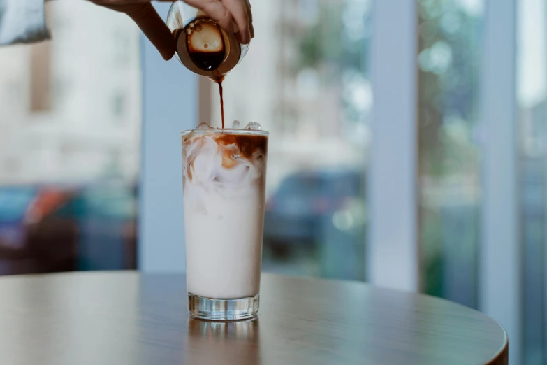 a person pouring a drink into a tall glass, unsplash, brown and cream color scheme, milkman, manuka, multiple stories