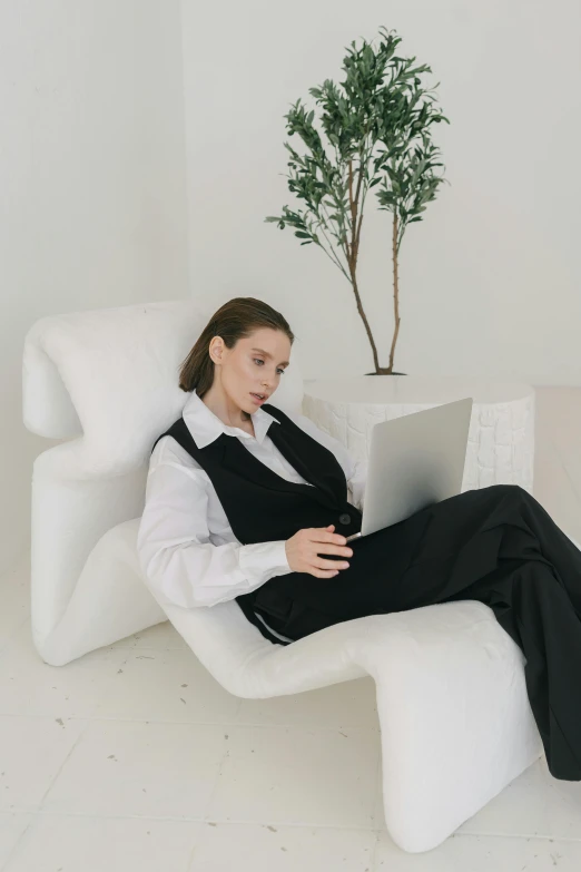 a woman sitting in a chair with a laptop, inspired by Marina Abramović, trending on pexels, white waistcoat, androgyny, lounge, formal wear