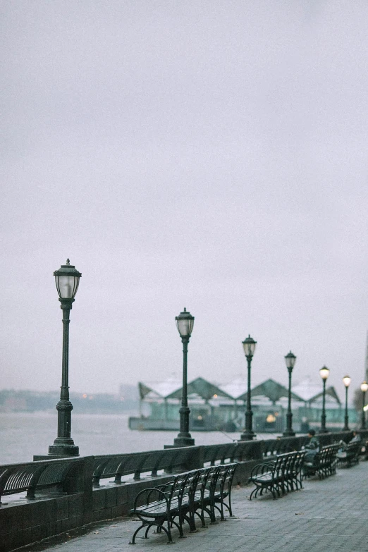 a couple of benches sitting next to each other on a sidewalk, inspired by Elsa Bleda, trending on unsplash, on liberty island, gas street lamps. country road, docked at harbor, gray sky