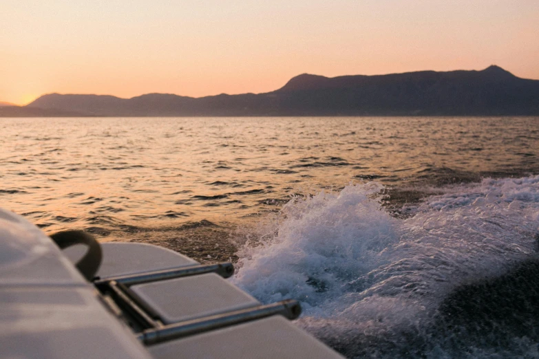 a boat on a body of water with mountains in the background, by Niko Henrichon, going forward to the sunset, croatian coastline, golden hour photograph, rear-shot