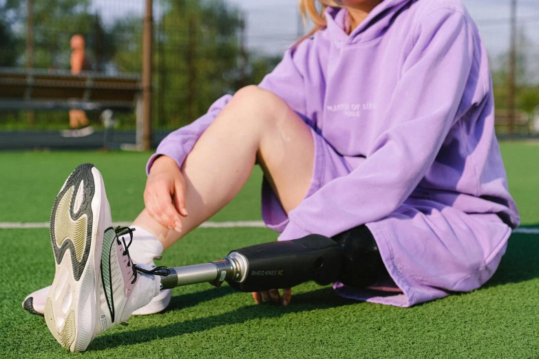 a woman sitting on top of a tennis court holding a racquet, unsplash, photorealism, wearing a purple sweatsuit, one legged amputee, wearing skirt and high socks, wearing bionic implants