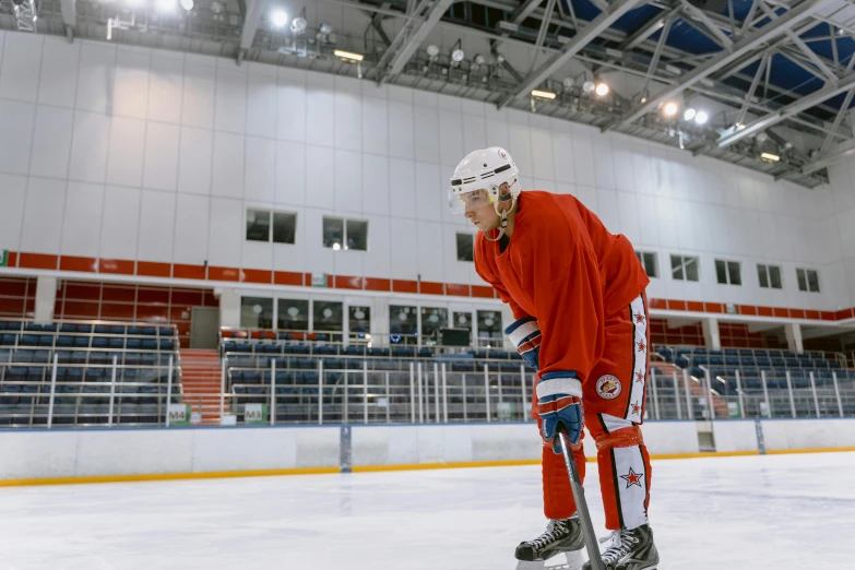 a man standing on top of an ice rink holding a hockey stick, a portrait, by Ilya Ostroukhov, shutterstock, wearing a red captain's uniform, practice, novi stars, a wide shot