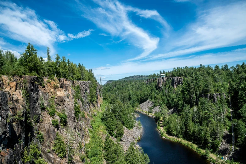 a river running through a lush green forest, by Jesper Knudsen, pexels contest winner, les nabis, rocky cliff, blue sky, quebec, thumbnail