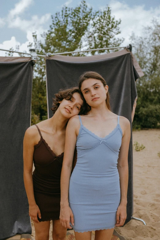 two women standing next to each other on a beach, an album cover, by Elsa Bleda, wearing a camisole, wearing a blue dress, fair olive skin, sleeveless tops