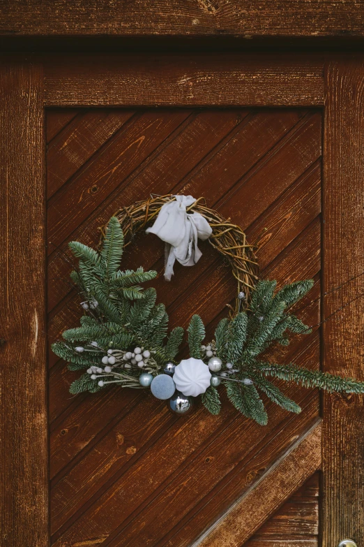 a close up of a wreath on a wooden door, a still life, inspired by Károly Markó the Elder, pexels contest winner, silver and cool colors, (3 are winter, minimalist, handcrafted