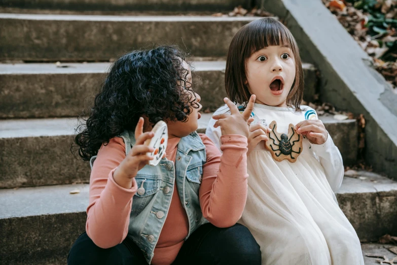 two little girls sitting next to each other on some steps, pexels contest winner, eating cakes, white prosthetic eyes, mixed race, woman holding another woman