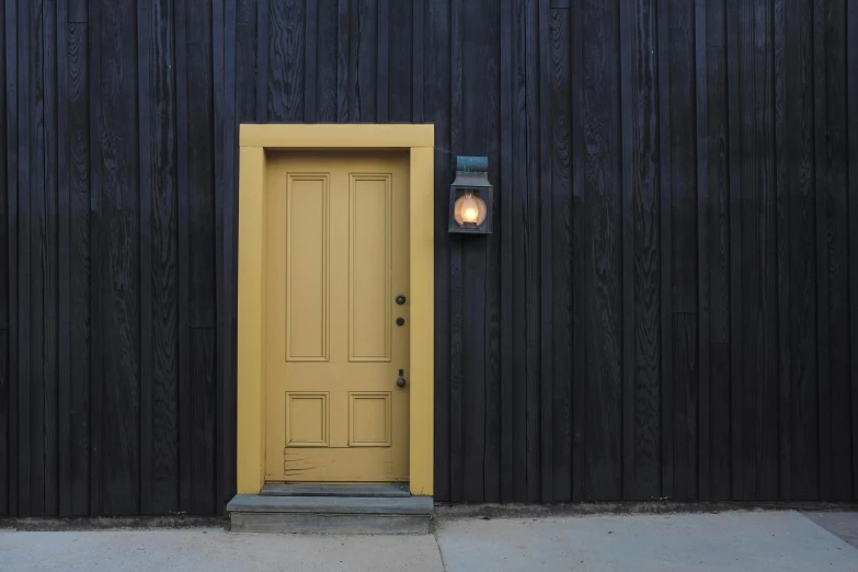 a yellow door in front of a black building, inspired by Gertrude Abercrombie, pexels contest winner, wood paneling, lantern light, brown, dwell