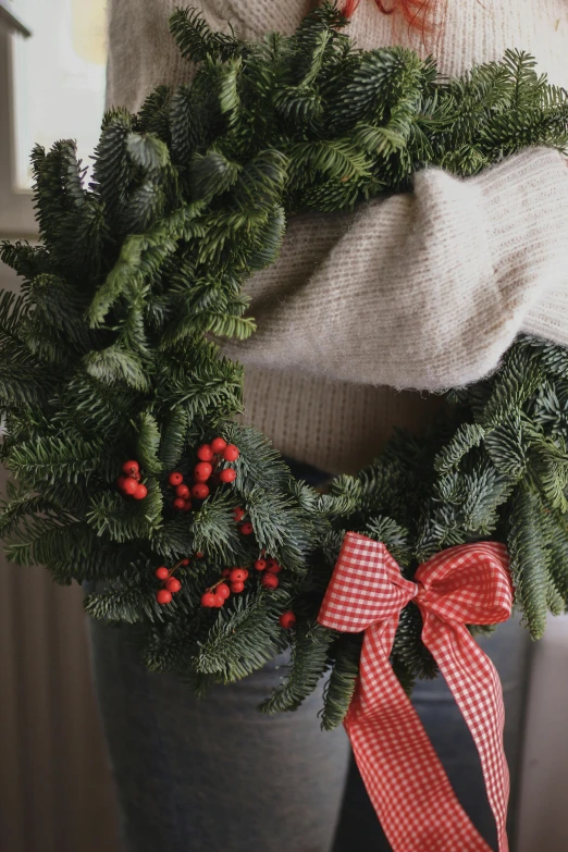 a close up of a person holding a wreath, cozy setting, uncropped, evergreen, ribbon